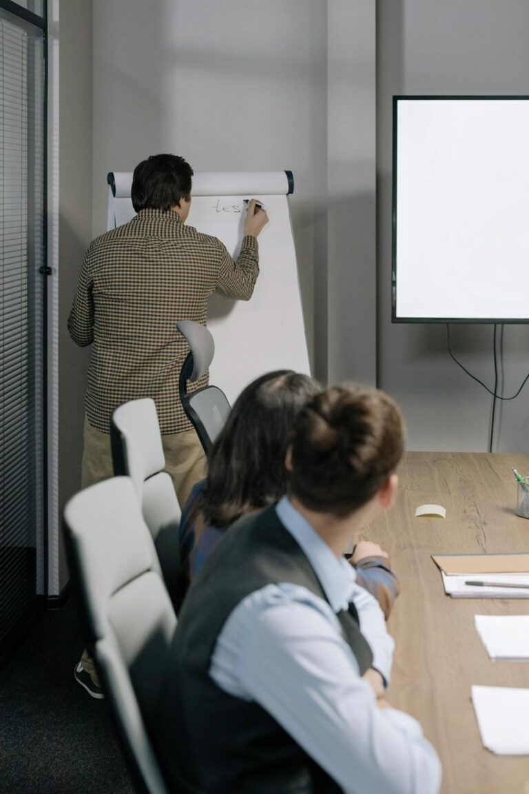 Three colleagues collaborating during an office meeting with a whiteboard discussion.