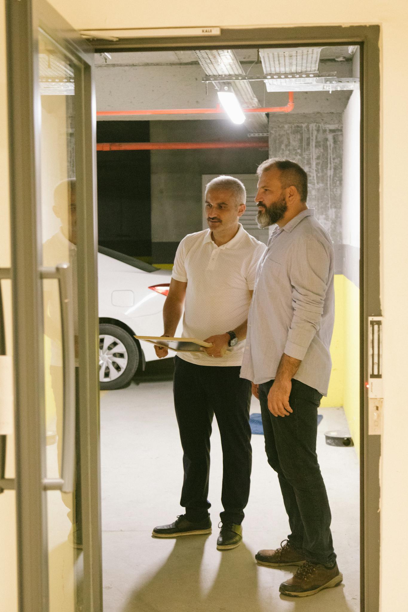 Two men in a parking garage reviewing documents near an open door.